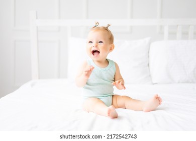 A cute little baby in a bodysuit made of natural cotton fabric is sitting on white bed linen in the bedroom. A happy little baby in bed. Textiles and bed linen for children. - Powered by Shutterstock