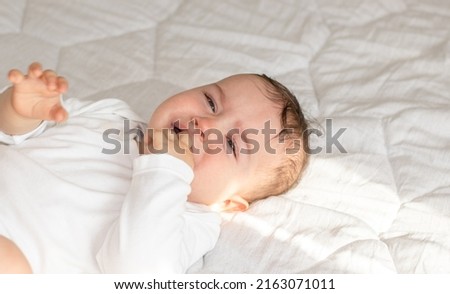 cute little baby boy is crying. toddler on bed, white blanket,sunny rays, morning situation.motherhood. teething period,bloating belly pain, want to sleep,eat, hungry child