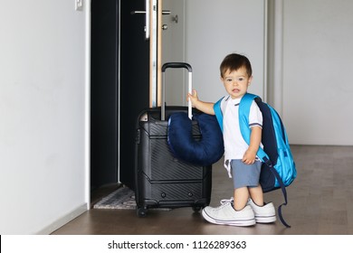 Cute Little Baby Boy In Fathers Shoes And With Big Backpack Holding Suitcase Staying Near Open Door Ready To Travel Leaving Home. Traveling With Child Concept