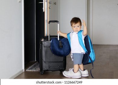 Cute Little Baby Boy In Fathers Sneakers And With Big Backpack Holding Suitcase And Waving Goodbye Staying At Open Door Ready To Travel. Traveling With Child Concept.