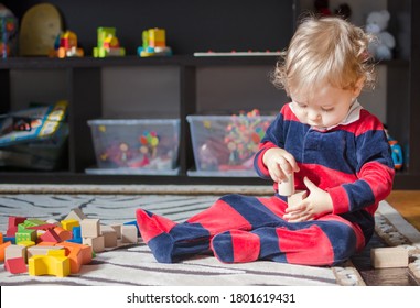 Kleiner kleiner Baby-Junge, der sich zu Hause amüsiert und mit bunten Holzblöcken auf dem Boden spielt.