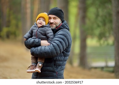 Cute little baby boy in his fathers arms. Dad and son having fun on cold autumn day in city park. Adorable son being held by his daddy.