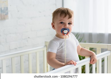 cute little baby boy with pacifier in baby crib looking at camera at home