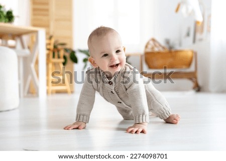 cute little baby boy in a pastel wool knitted suit learning to crawl on the floor in a bright living room, baby smiling, playing, early development of children