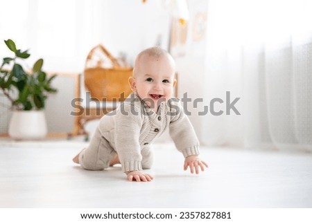 cute little baby boy in a pastel wool knitted suit learning to crawl on the floor in a bright living room, baby smiling, playing, early development of children