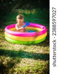 A cute little baby boy is playing with toys while bathing in a little colorful wading pool on meadow garden field outdoor. Summer time. Joy and happiness. Love and family 