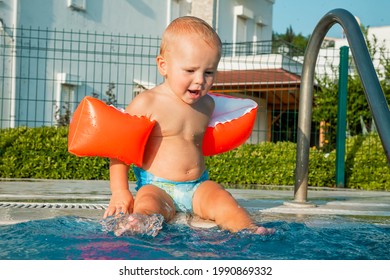 Cute little baby boy playing in outdoor swimming pool on hot summer day. Kids learn to swim. Happy child with orange floaties. Swimming aid protection for kid. Family summer vacation.