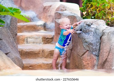 Cute little baby boy playing with water splashes and tap in a swimming pool on a sunny hot summer day