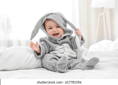 Cute Little Baby In Bunny Costume Sitting On Bed At Home