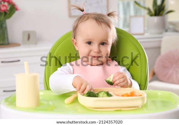 Cute little\
baby eating food in high chair at\
home