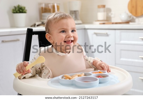 Cute\
little baby eating food in high chair at\
kitchen