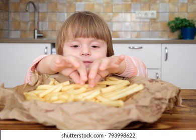 Cute little baby girl enjoying french fries on kitchen