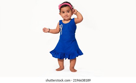 Cute Little Baby Girl Standing Pose, One Hand At Hair And Wearing Blue Frock, Isolated On White Background