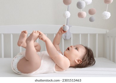 Cute little baby looking at hanging mobile in crib
