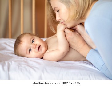 Cute Little Baby And Loving Mother, Closeup, Side View. Affectionate Blonde Woman Kissing And Cuddling With Her Smiling Awaken In Wooden Crib Toddler, Copy Space. Motherhood, Parenthood Concept