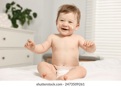 Cute little baby with moisturizing cream on face sitting on bed at home - Powered by Shutterstock