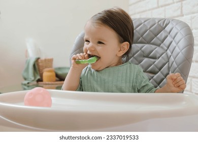 Cute little baby nibbling teether in high chair indoors. Space for text