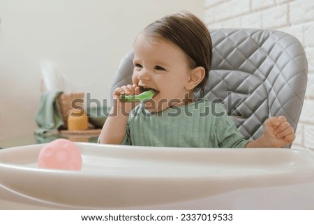 Cute little baby nibbling teether in high chair indoors. Space for text