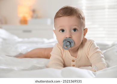 Cute little baby with pacifier on bed indoors