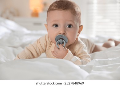 Cute little baby with pacifier on bed indoors