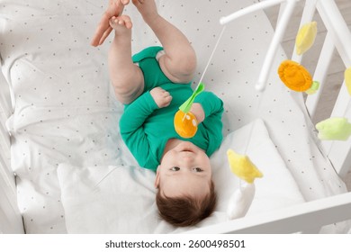 Cute little baby playing with cot mobile in crib at home