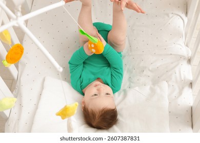 Cute little baby playing with cot mobile in crib at home, closeup