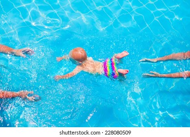 Cute little baby swimming underwater from mother to father in a pool, learning to swim lessons and early development concept