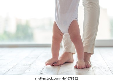 Cute Little Baby Is Toddling While Learning To Walk, Mom Is Holding His Hands, Cropped