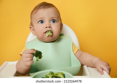 Cute Little Baby Wearing Bib While Eating On Yellow Background