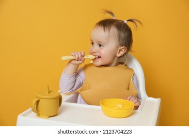 Cute Little Baby Wearing Bib While Eating On Yellow Background