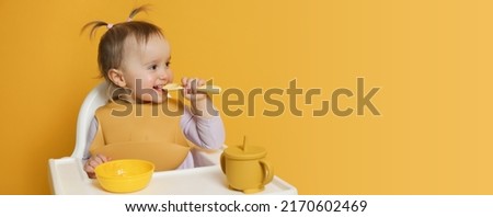 Cute little baby wearing bib while eating on yellow background, space for text. Banner design