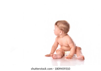 Cute Little Baby Wearing Diapers Portrait. Studio Shot Of Small Toddler Kid In Nappy Looking Back. Child Playing Seated On Floor Over White Background. Childcare And Innocence. Happy Babyhood