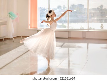 Cute Little Ballerina In White Ballet Costume And Pointe Shoes Is Dancing In The Room. Kid In  Dance Class. Child Girl Is Studying Ballet.  Copy Space.