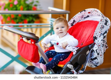 Cute little beautiful baby girl sitting in the pram or stroller and waiting for mom. Happy smiling child with blue eyes.