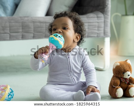 Cute little Black baby boy putting rattle toy into mouth.
