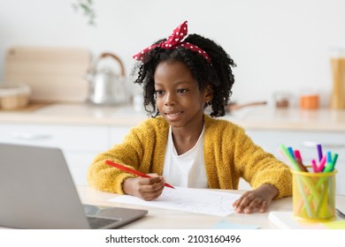 Cute Little Black Girl Drawing In Kitchen While Study Online With Laptop At Home, Smiling African American Female Child Doing Homework With Computer, Enjoying Distance Learning, Copy Space