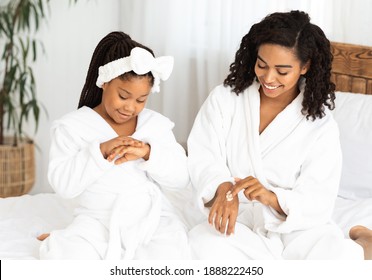 Cute Little Black Girl And Her Mom Applying Hand Cream At Home, Wearing Bathrobes. Loving African Mother And Her Child Having Domestic Spa Day, Enjoying Spending Time Together, Closeup Shot