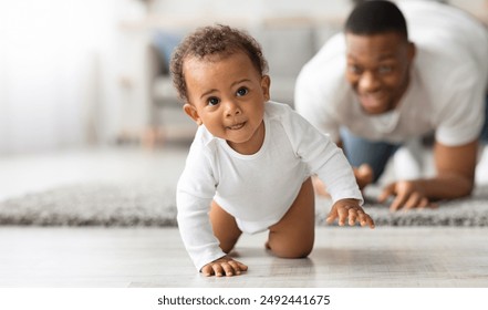 Cute Little Black Infant Baby Crawling On Floor At Home, Proud Young Father Looking At Him And Smiling, Dad And Toddler Child Enjoying Spending Time Together, Selective Focus With Copy Space - Powered by Shutterstock