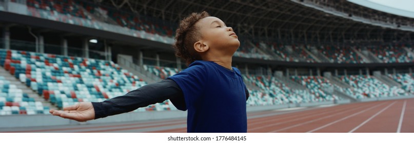 Cute Little Black Kid Boy Spreading His Hands On An Empty Stadium, Dreaming Of Becoming Professional Player, Soccer Star