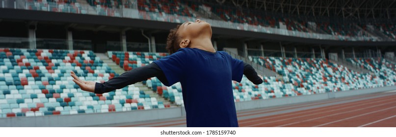 Cute Little Black Kid Boy Spreading His Hands On An Empty Stadium, Dreaming Of Becoming Professional Player, Soccer Star