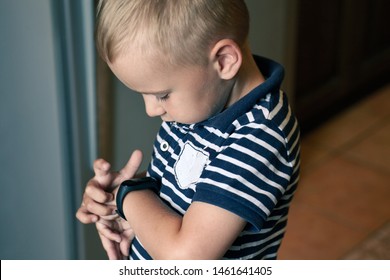 Cute little blond boy with blue eyes points out to digital fitness tracker on his wrist. Serious expression, strong emotions, children computerization concept. Indoors, dark background, copy space. - Powered by Shutterstock