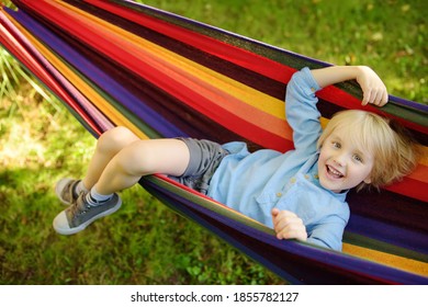 Cute Little Blond Caucasian Boy Relaxing And Having Fun In Multicolored Hammock In Backyard Or Outdoor Playground. Summer Active Leisure For Kids. Child Swinging On Hammock. Activities For Children