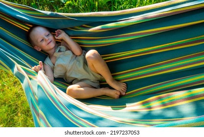 Cute Little Blond Caucasian Boy Having Fun With Multicolored Hammock In Backyard Or Outdoor Playground. Summer Active Leisure For Kids. Child On Hammock. Activities And Fun For Children Outdoors. 