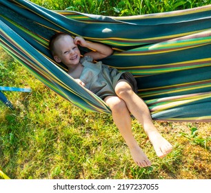 Cute Little Blond Caucasian Boy Having Fun With Multicolored Hammock In Backyard Or Outdoor Playground. Summer Active Leisure For Kids. Child On Hammock. Activities And Fun For Children Outdoors. 