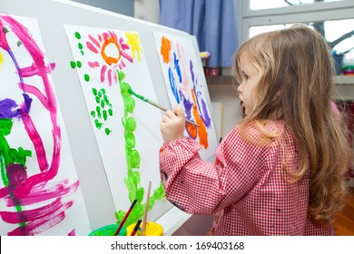 Cute little blond girl holding the brush and painting on the paper