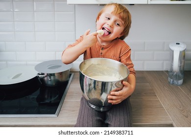 Cute Little Blond Preschool Kid Boy Baking Cake In Domestic Kitchen, Indoors. Laughing Child  Tasting Sweet Dough. Little Helper
