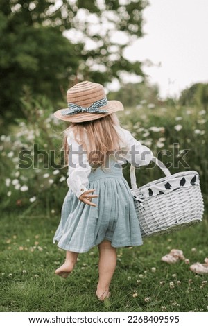 Cute little blonde girl in a cotton dress and straw hat walks in