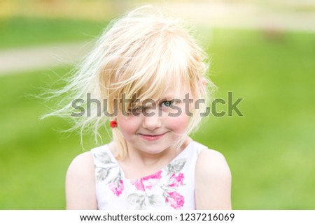 A cute little blonde girl with messy hair pulls a funny face, being cheeky