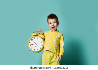 Cute little boy with alarm clock,isolated on blue. Funny kid yawning pointing at alarm clock at morning. Excited boy overslept before school. People, school, time and lifestyle concept