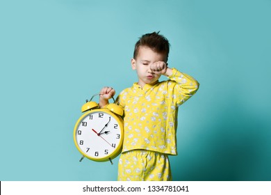 Cute little boy with alarm clock,isolated on blue. Funny kid yawning pointing at alarm clock at morning. Excited boy overslept before school. People, school, time and lifestyle concept